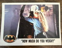 A photo of a trading card with a still from a Batman movie. Batman is holding on to a rope while a woman holds on to him. At the bottom of the card is the text ‘How much do you weigh?’